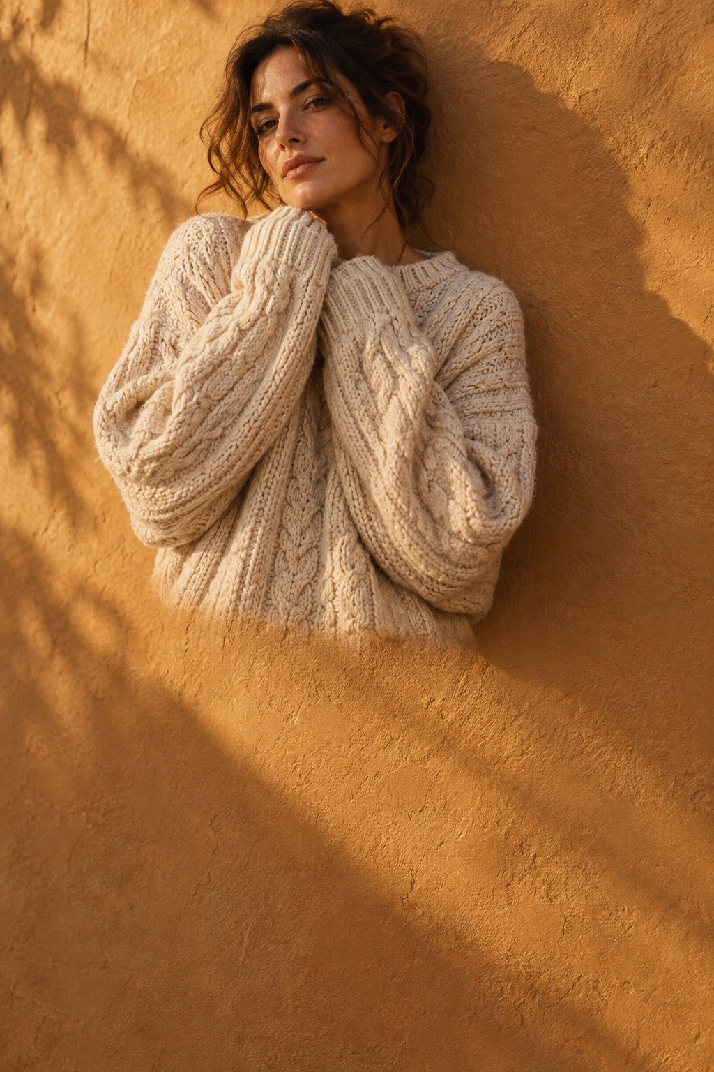 Femme en pull en maille crème devant un mur ocre